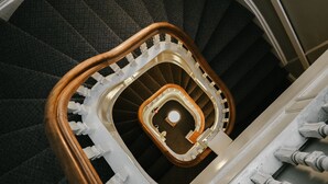 Una escalera de caracol con barandilla de madera y balaustres blancos, que conduce a un rellano con plataforma circular.