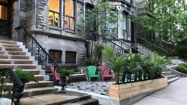 Un edificio histórico con fachada de piedra, una escalera que conduce a la entrada y asientos exteriores con sillas.