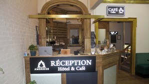 Un mostrador de recepción con un cartel que dice 'RECEPTION Hôtel & Café', una computadora portátil y una planta en maceta.