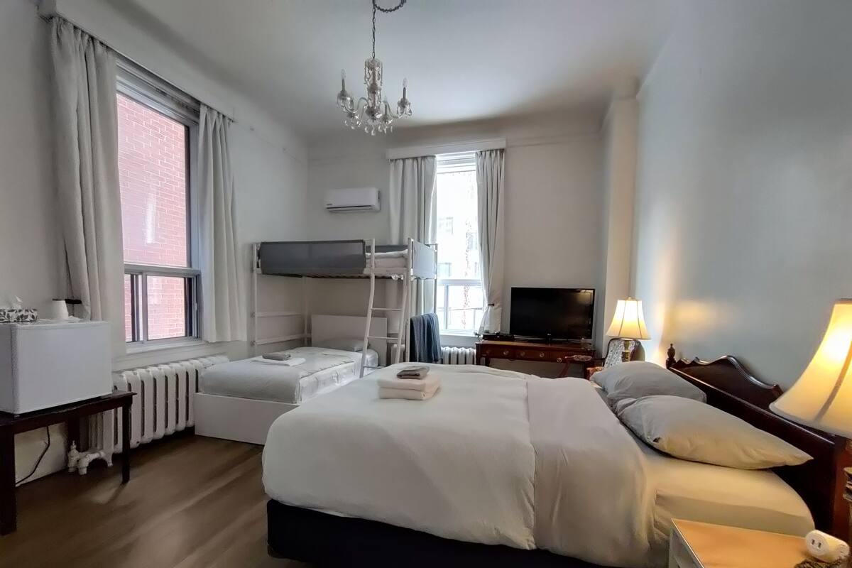 A hotel room with a bunk bed, a flat-screen TV, a desk with a lamp, and a chandelier.