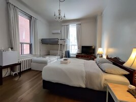 Une chambre d’hôtel avec un lit superposé, un téléviseur à écran plat, un bureau avec une lampe et un lustre.