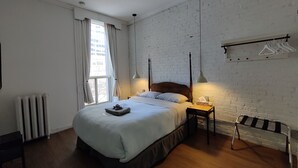 Un dormitorio con una cama grande, un radiador, una ventana con cortinas, una lámpara colgante y un perchero con ganchos.
