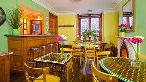 Un comedor con una decoración en tonos verde y amarillo, que incluye una mesa redonda grande con sillas, una barra con taburetes y una chimenea con un espejo encima.