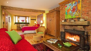 Una habitación acogedora con un sofá rojo, una mesa de centro de madera, una chimenea y una cama con colcha roja.