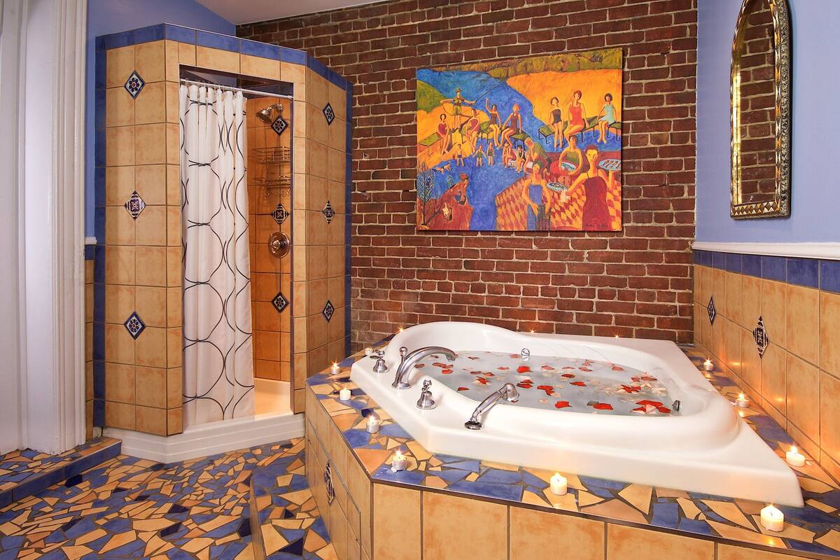 Un baño con una bañera grande, zona de ducha y suelo de mosaico.