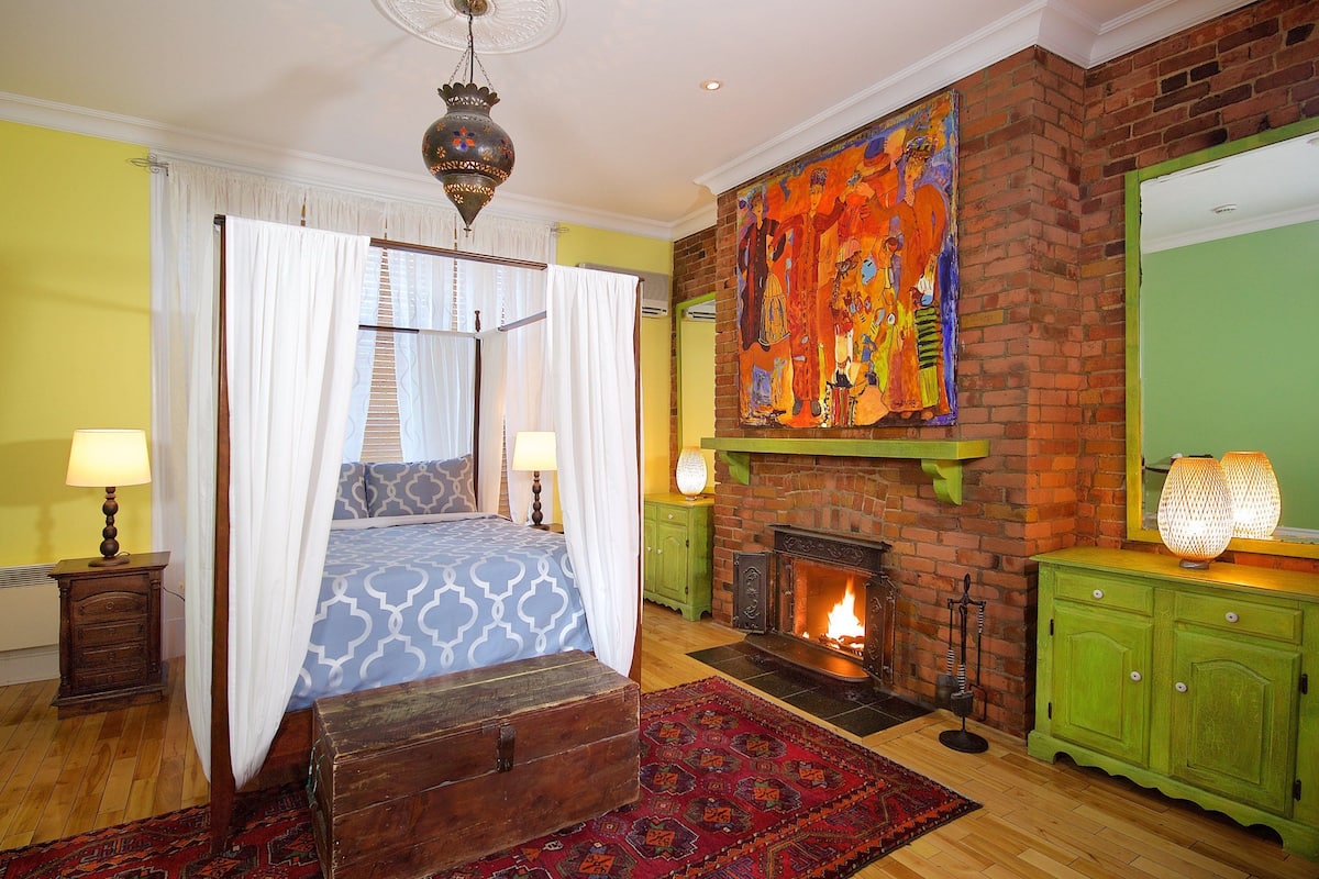 Un dormitorio con cama con dosel, chimenea, un mural grande y un armario verde.