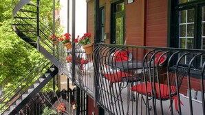 Un balcón con escalera espiral, asientos exteriores rojos y plantas en macetas.