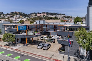 A multi-story hotel with a blue sign reading "BECK'S Motor Lodge" on the ground floor. There are several cars parked in the driveway, and a flagpole with a rainbow flag is visible.