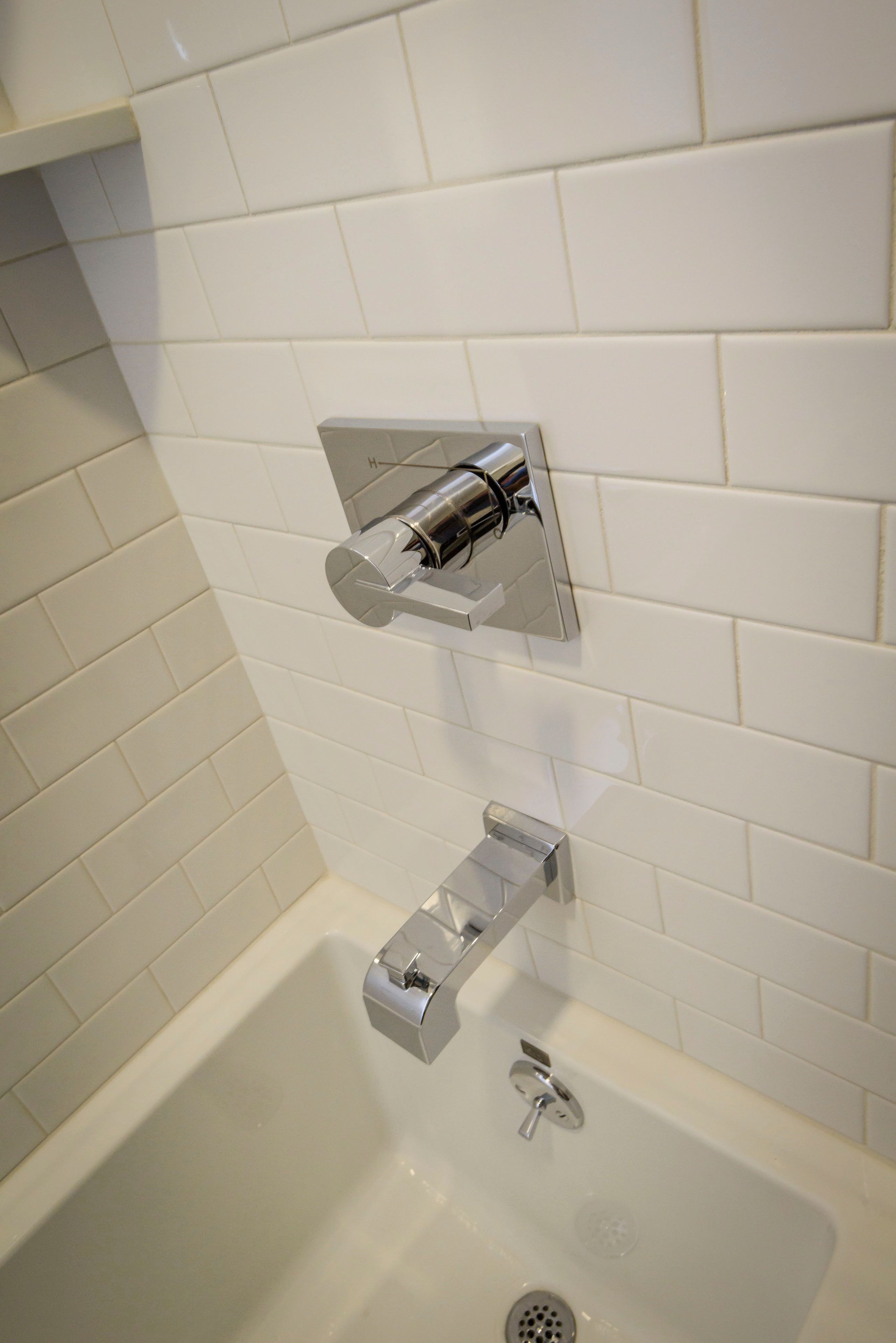 A modern bathroom with white tiles, a chrome showerhead, and a separate hand shower.