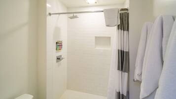 Un baño moderno con paredes de azulejos blancos, zona de ducha, inodoro y un perchero con toallas.