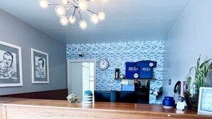 Zona de recepción con mostrador de madera, un reloj, cuadros enmarcados, pared azul con diseño en zigzag y un letrero que dice 'Welcome'.