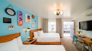Habitación de hotel con dos camas, un escritorio, un televisor y un balcón con vistas a edificios.
