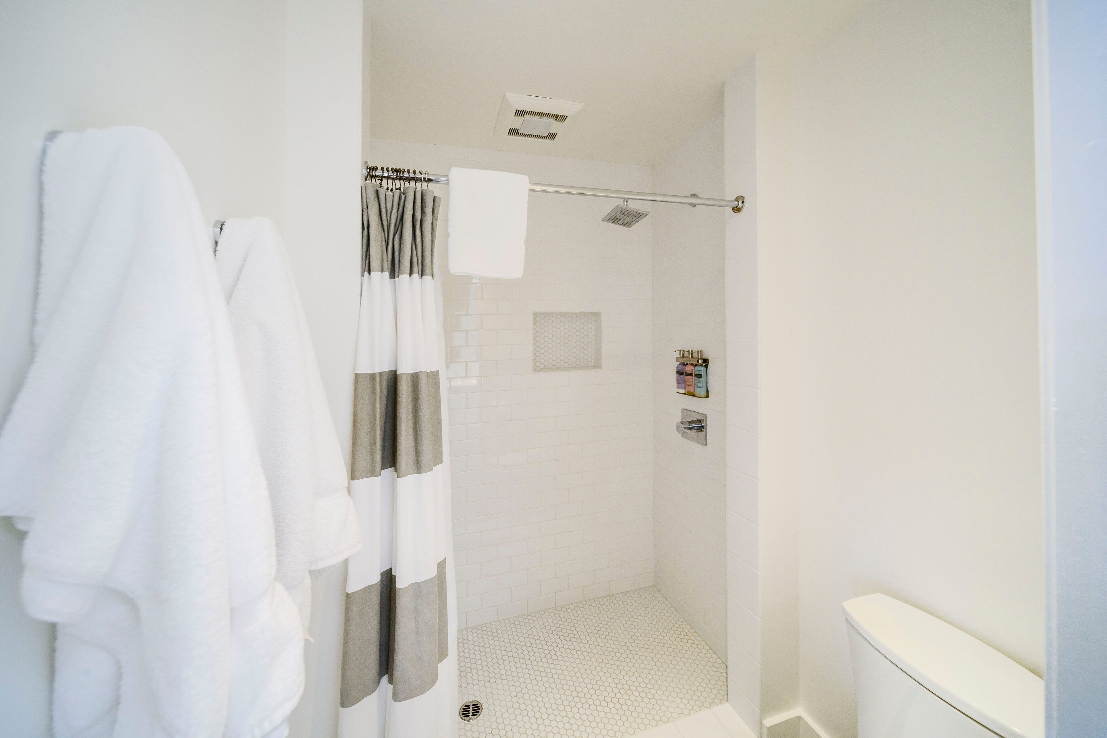 A modern bathroom with a shower, white tiles, a towel rack, and a toilet.