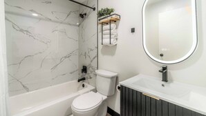 A bathroom with a marble wall, a toilet, a bathtub, a sink, and a mirror.