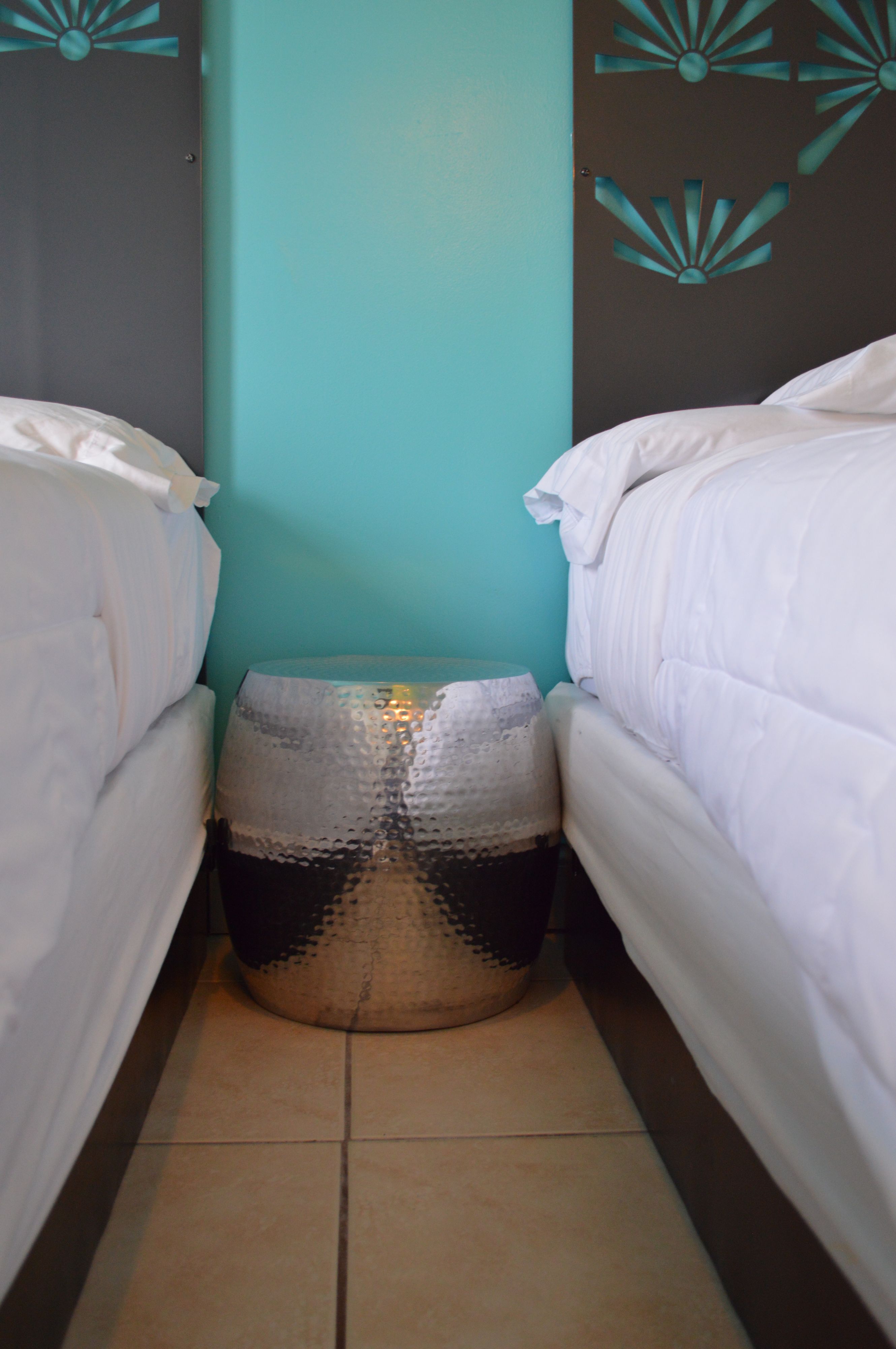 Een smalle hotelkamer met twee bedden, een muur in turquoise en een ronde tafel met een structuur.