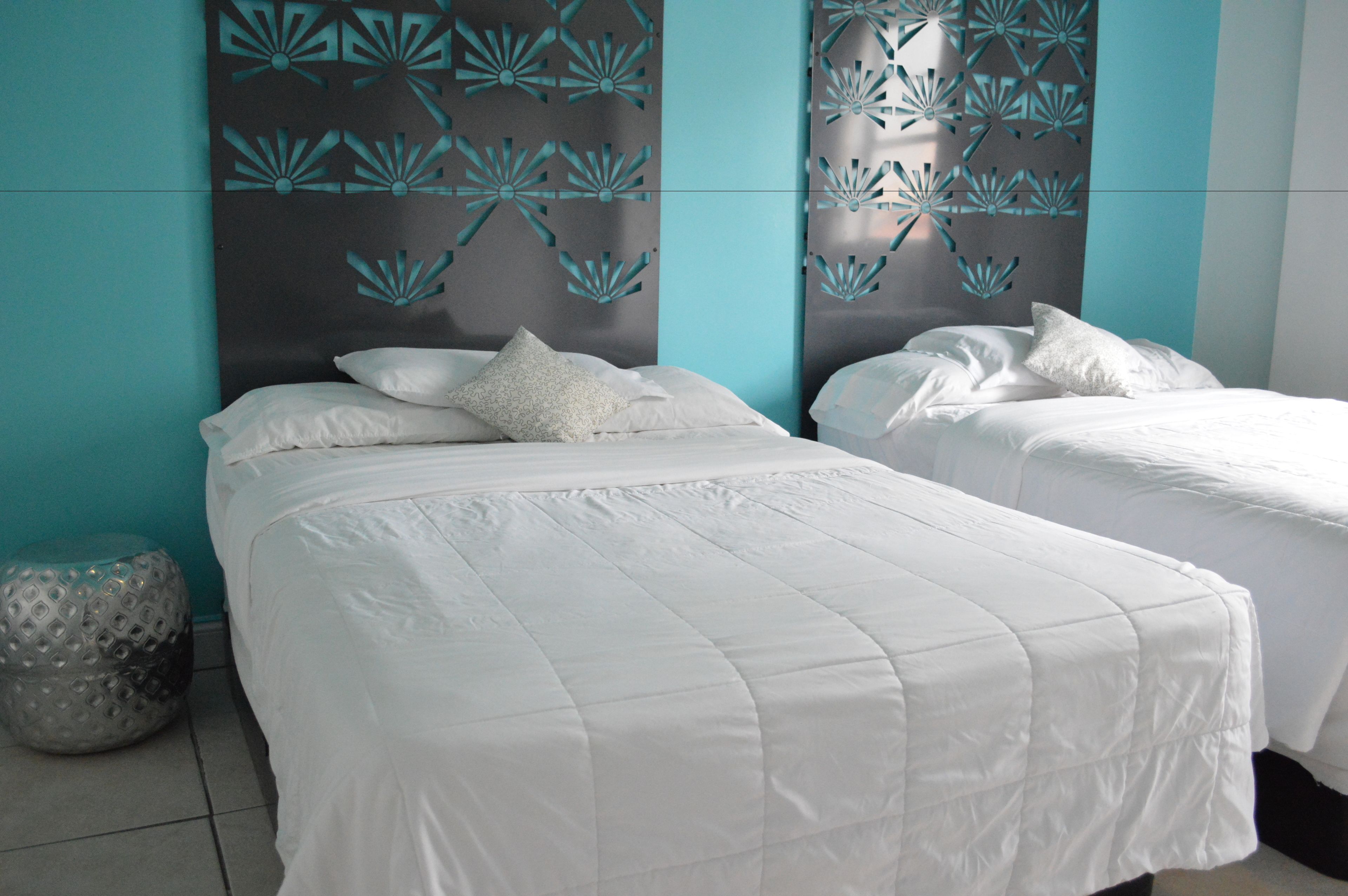 A hotel room with two beds, a decorative wall panel, and a textured floor lamp.