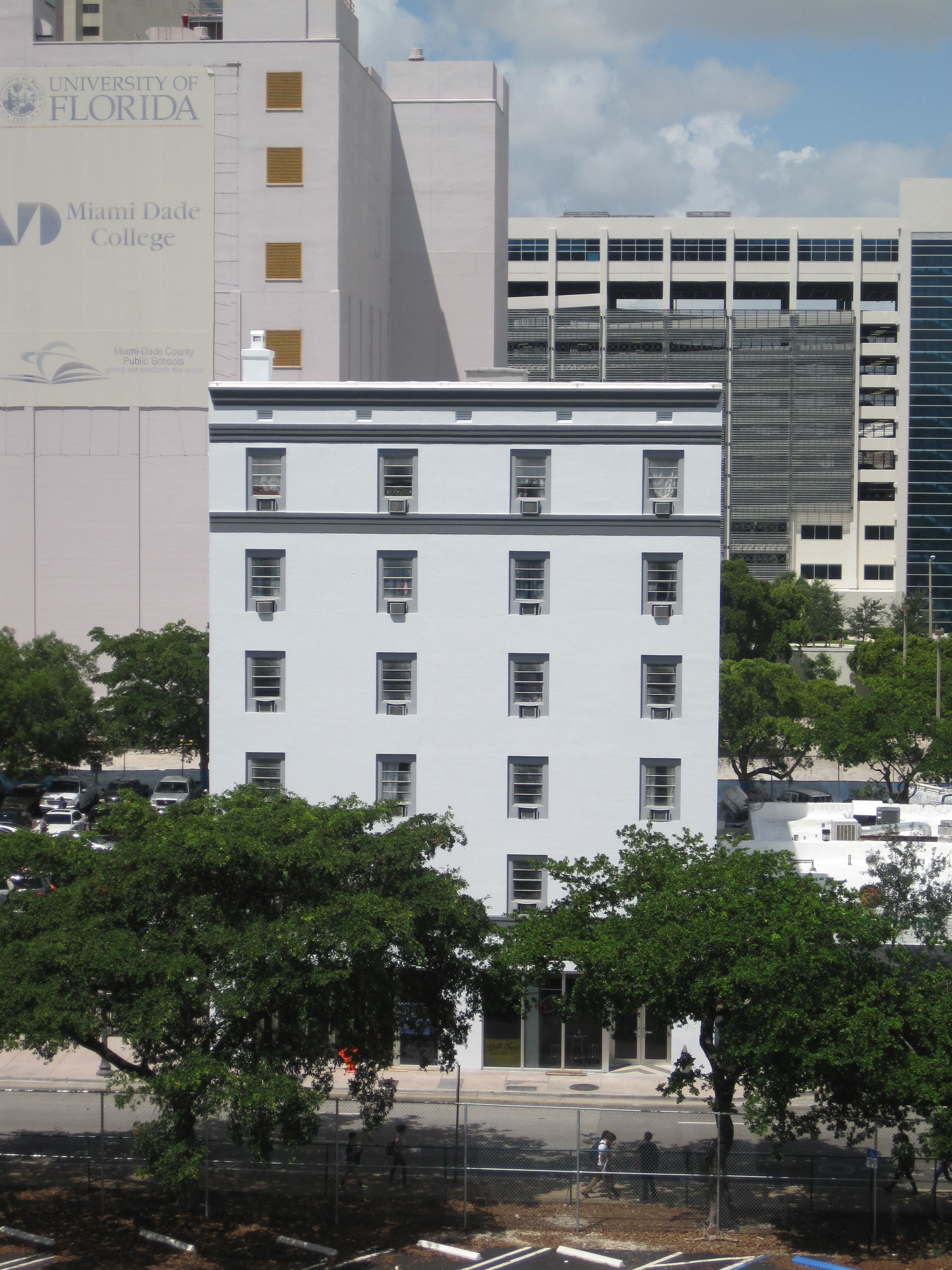 A white building with multiple windows and air conditioning units, surrounded by trees and a fence.