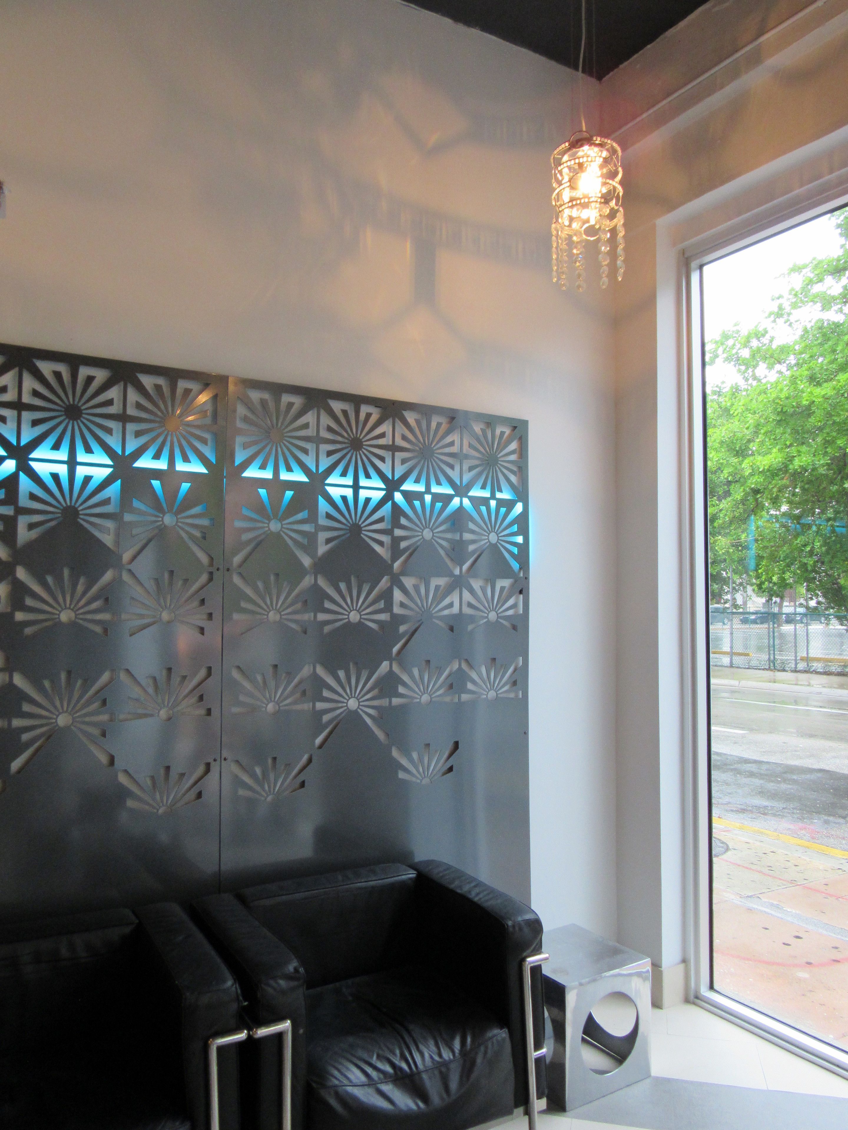 A modern interior with a black leather sofa, a decorative metal wall panel, and a hanging light fixture.