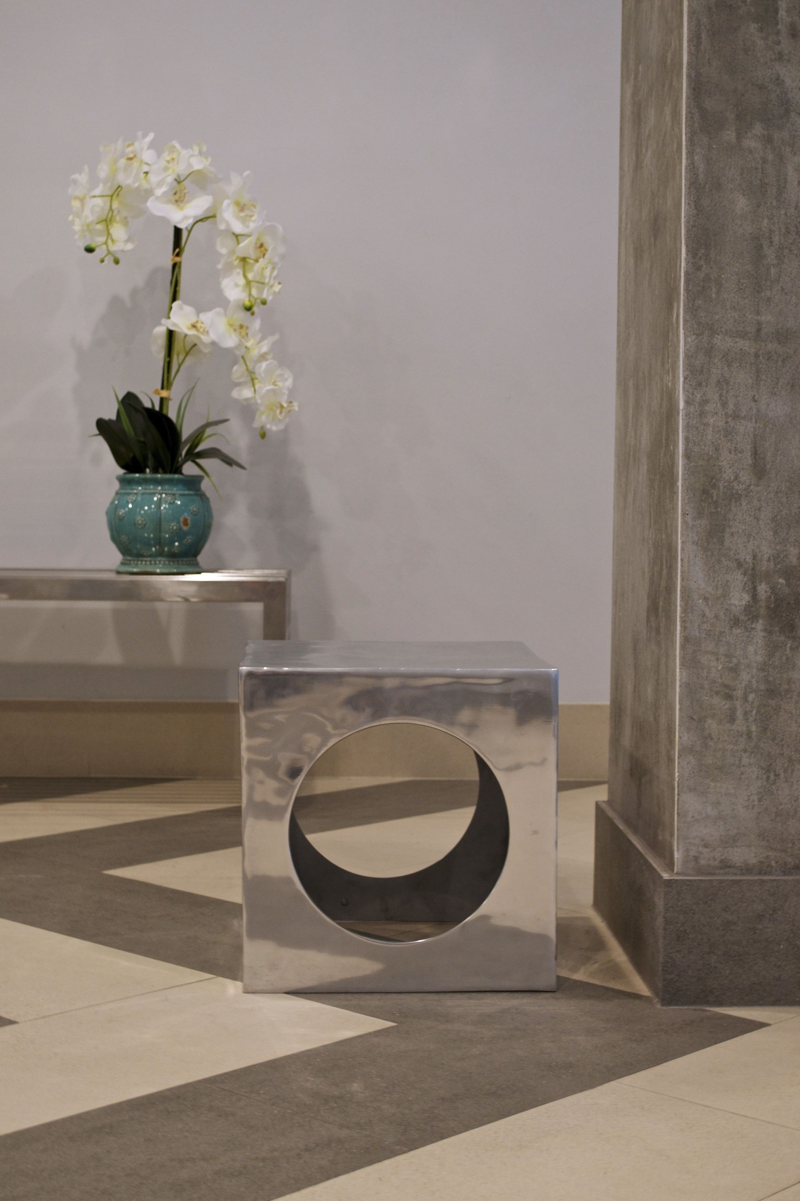 A modern interior with a metallic cube-shaped object and a potted orchid on a bench.