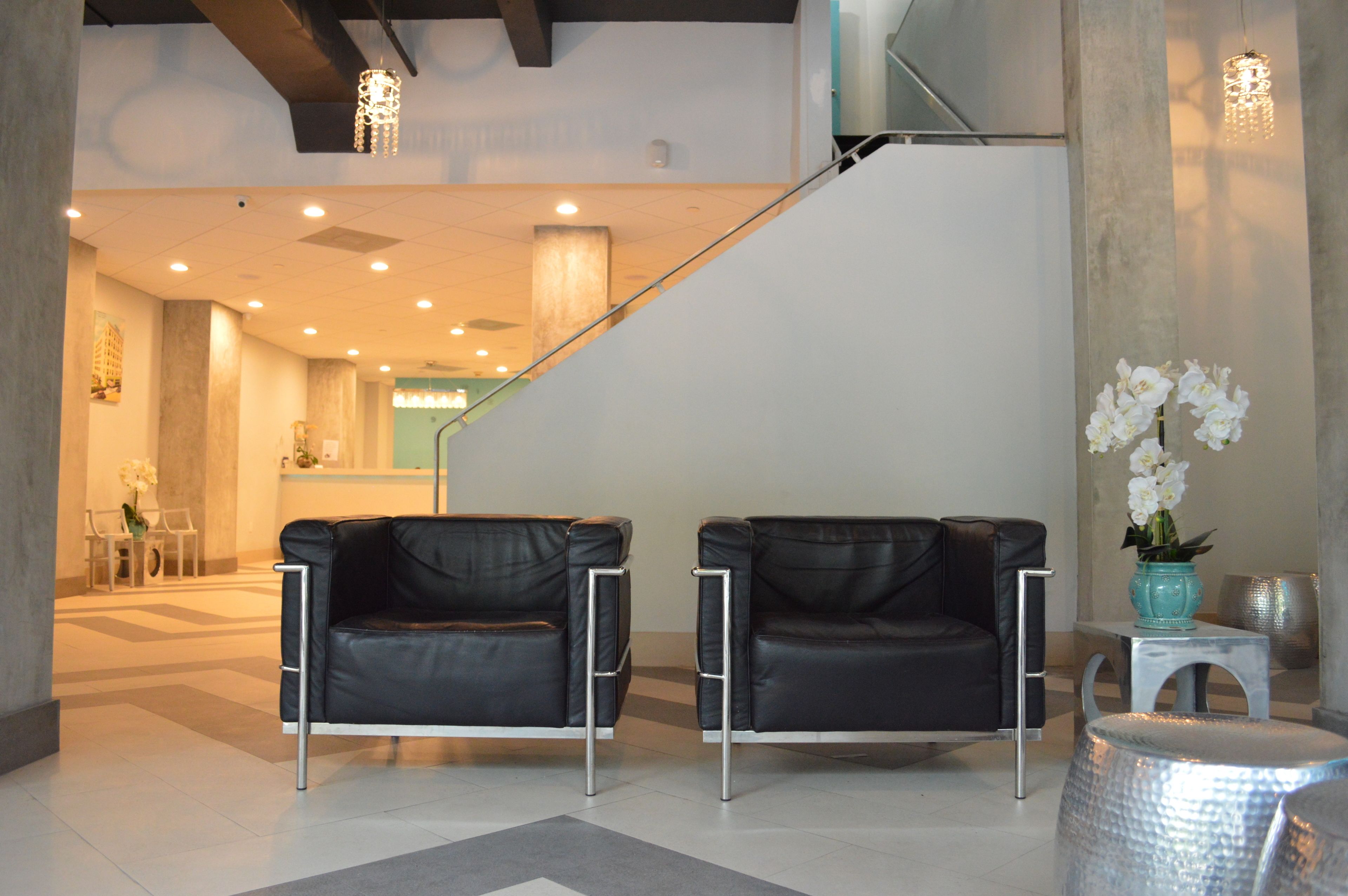 A modern lobby with a staircase, two black leather sofas, a small table with a vase of flowers, and a metal stool.