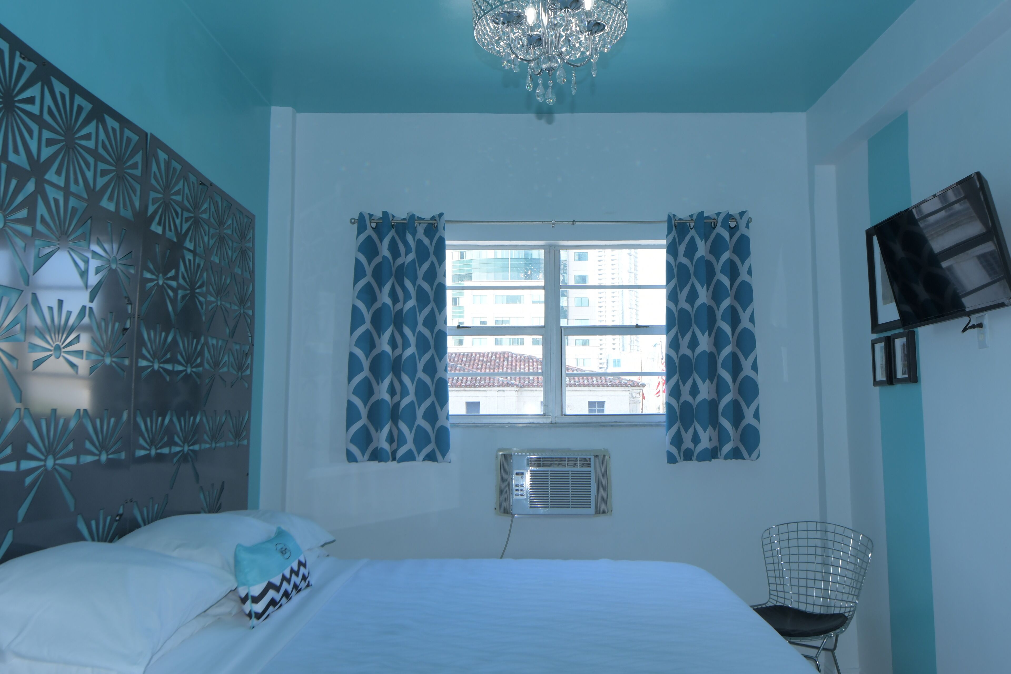A bedroom with a bed, curtains, a TV, and a decorative wall panel.