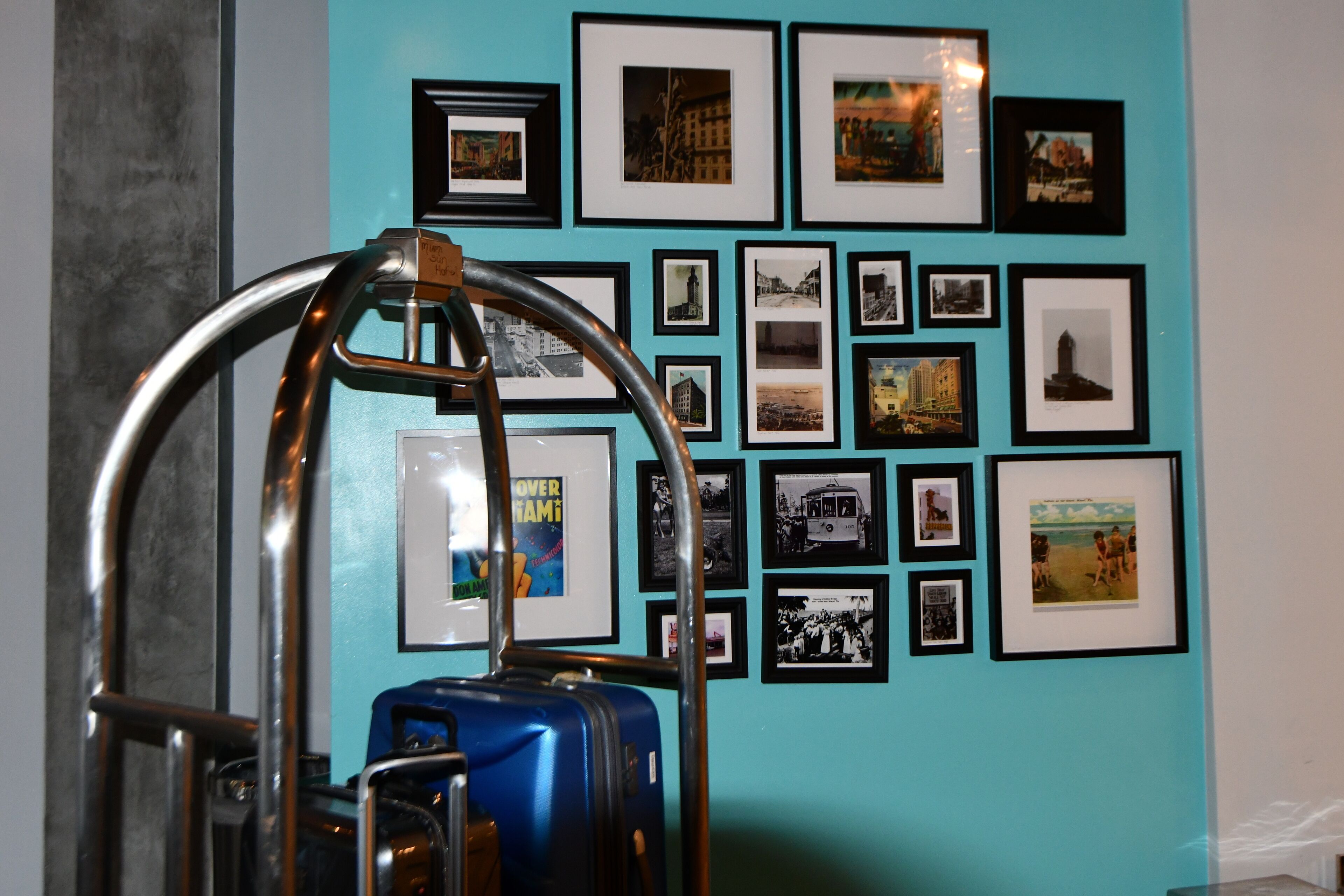 Un mur orné de plusieurs photographies encadrées, avec une valise bleue placée au premier plan.