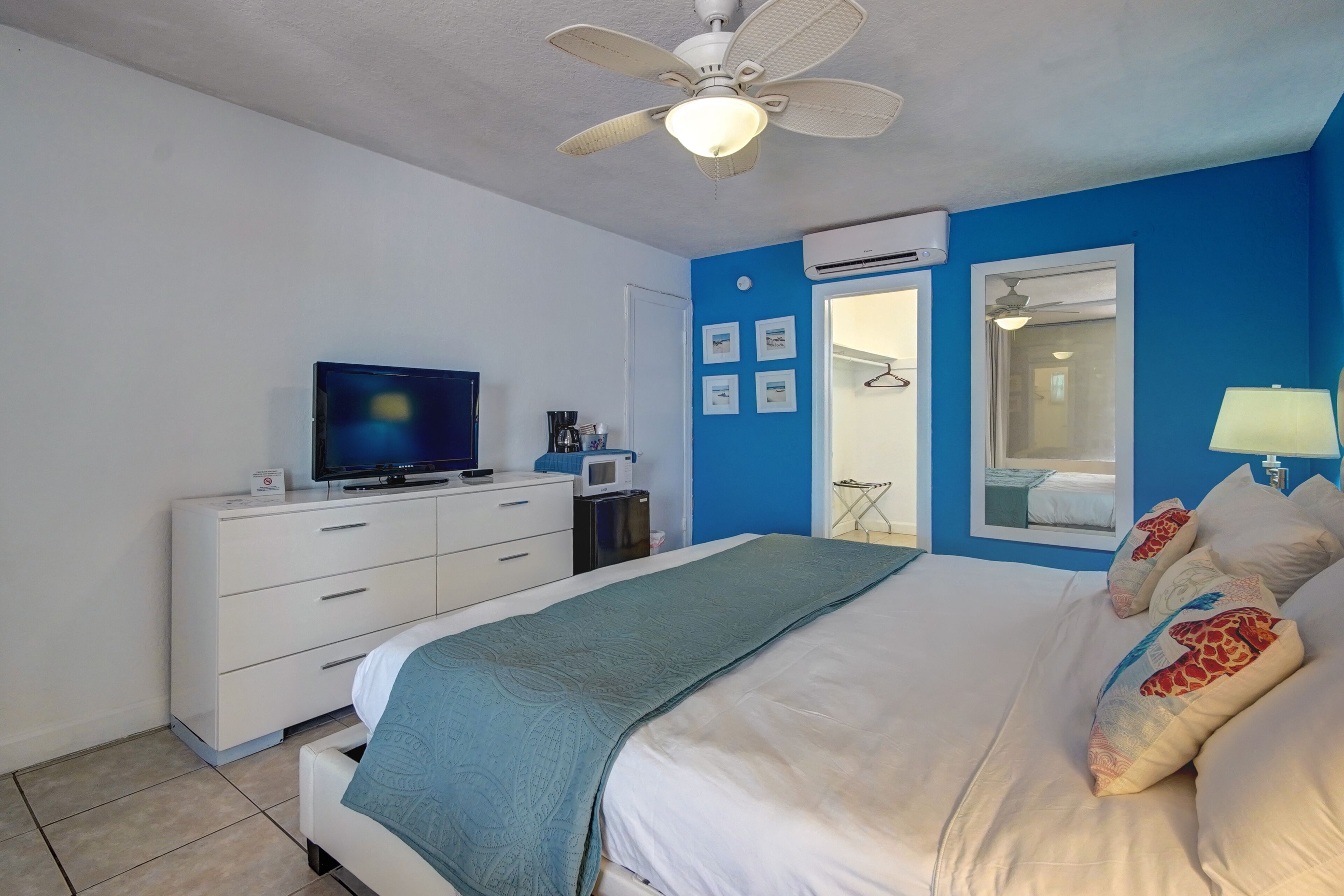 A bedroom with a bed, a TV, a desk, and a ceiling fan.