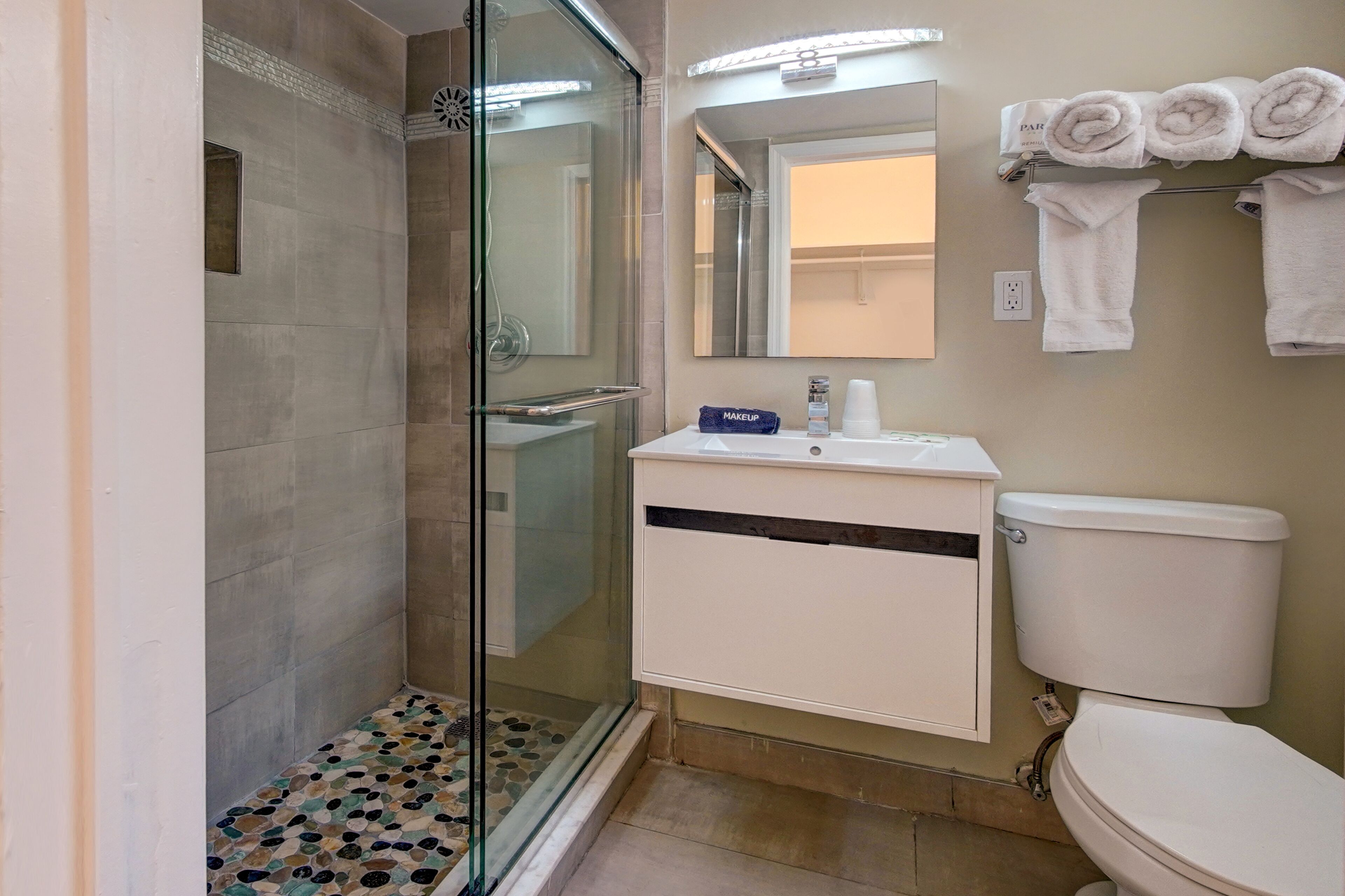 Une salle de bain avec une douche à parois de verre, un lavabo blanc avec un miroir au-dessus et des toilettes.