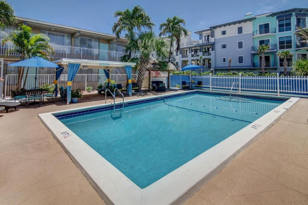 A rectangular pool with a white border, surrounded by a white fence, and a palm tree in the background.