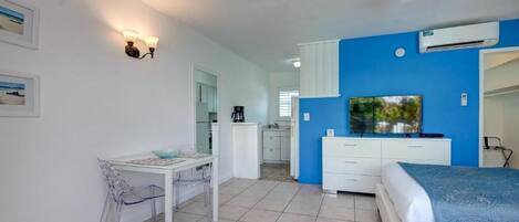 Une chambre à coucher comprenant un lit, un bureau, une chaise, un ventilateur de plafond et un téléviseur.