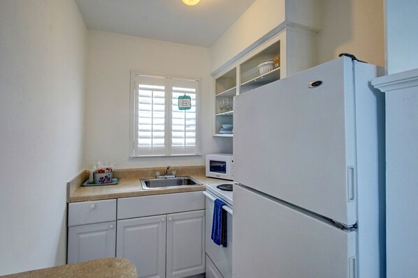 A compact kitchen with white cabinets, a sink, a microwave, and a refrigerator. - Castle by the Sea (Lauderdale-by-the-Sea)