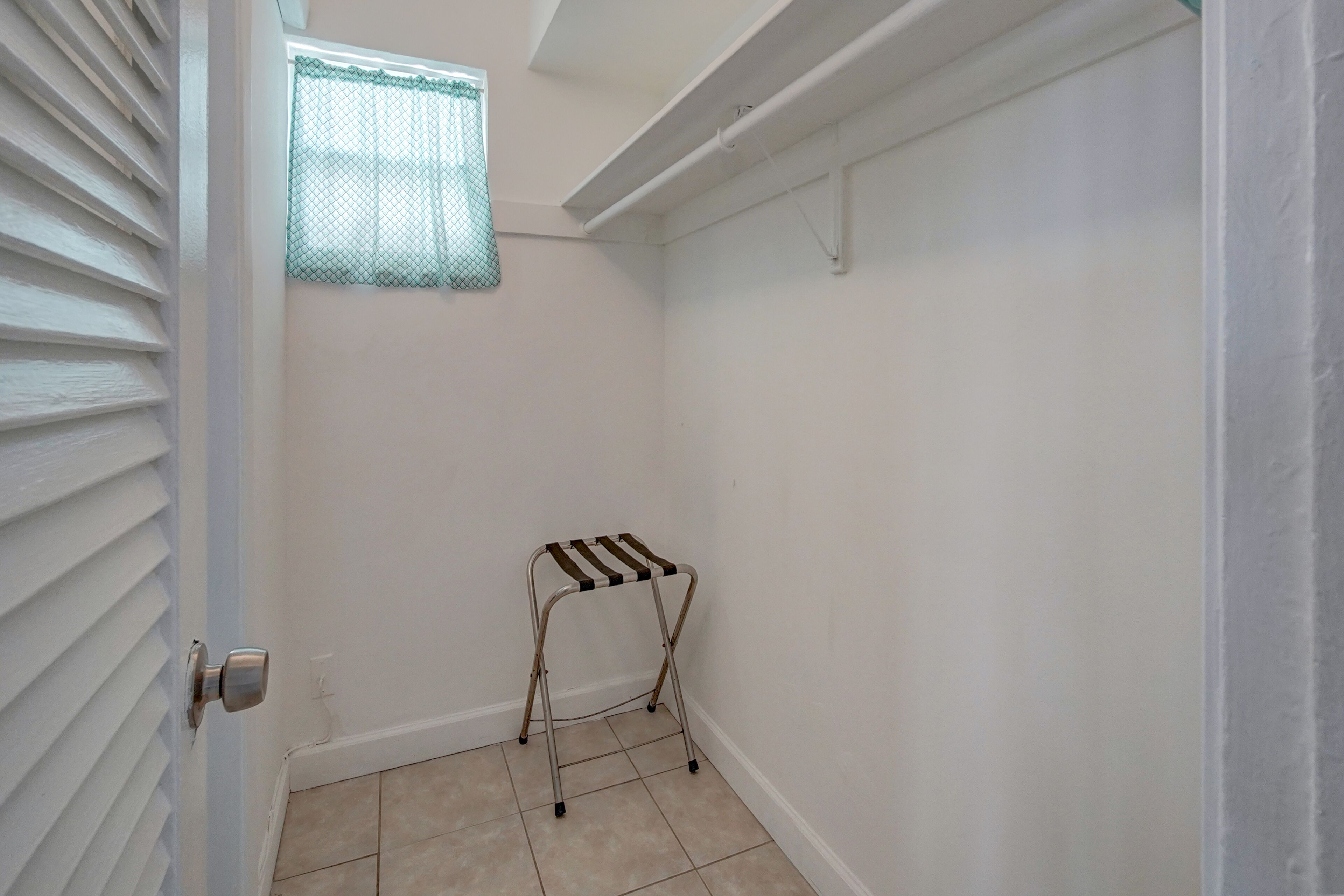 A small, clean room with a metal folding chair, a window with a mesh screen, and a door with a silver handle.