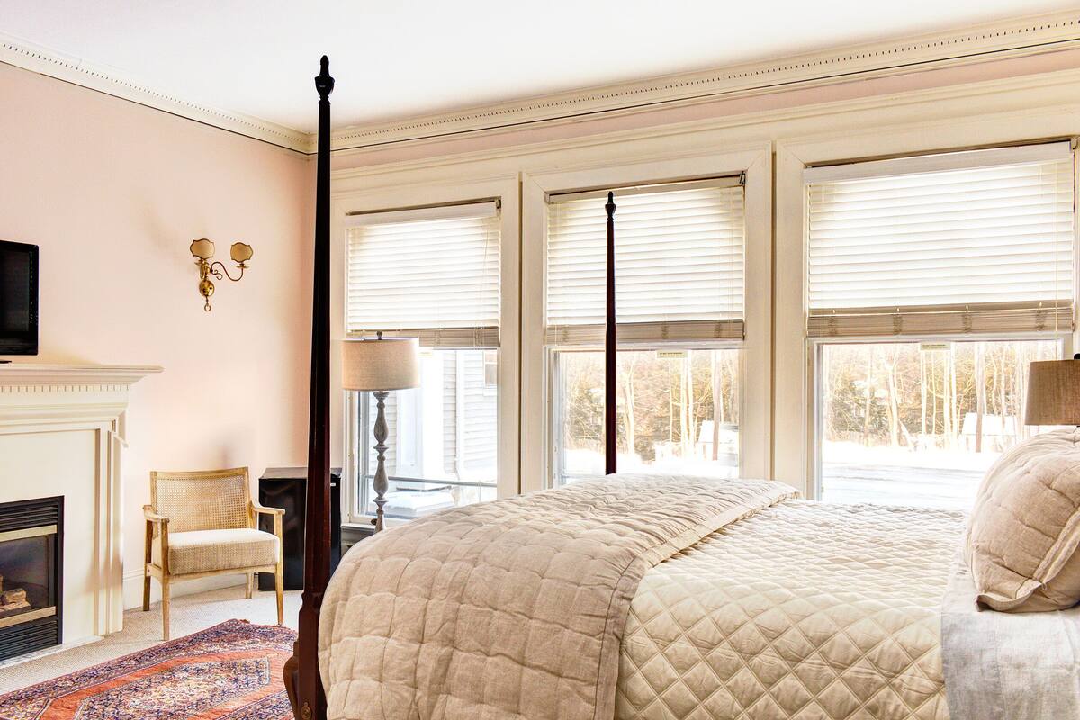 A bedroom with a large bed, a fireplace, a chair, and a television.