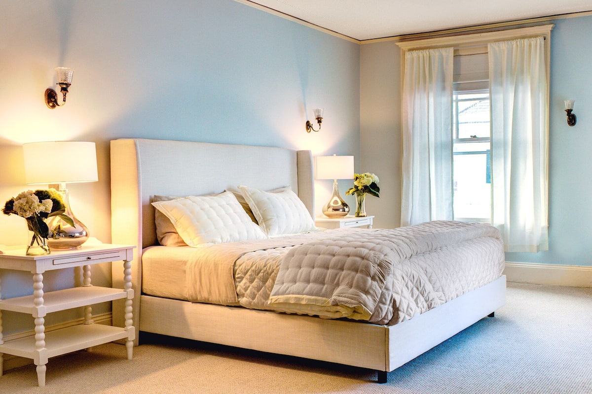 A bedroom with a bed, nightstands, lamps, and a window with curtains.