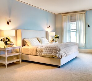 A bedroom with a bed, nightstands, lamps, and a window with curtains.
