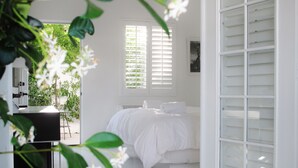 A bedroom with a bed, white walls, and a window with blinds. - Alcazar Palm Springs (Palm Springs)