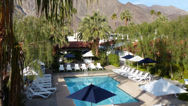 A pool area with lounge chairs and umbrellas, surrounded by palm trees and mountains in the background. - Alcazar Palm Springs (Palm Springs)