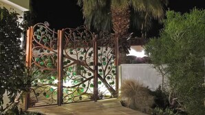 A gated entrance with a decorative metal fence featuring green leaves and a palm tree. - Alcazar Palm Springs (Palm Springs)