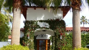 A building entrance with a white facade, a wooden door, and a covered walkway. - Alcazar Palm Springs (Palm Springs)
