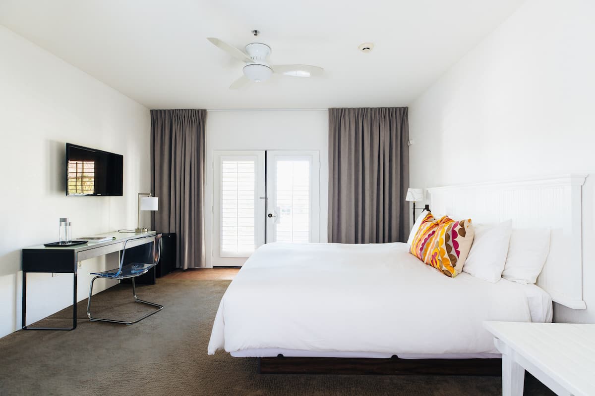 Habitación de hotel con una cama, un escritorio con una silla, un televisor y un ventilador de techo.