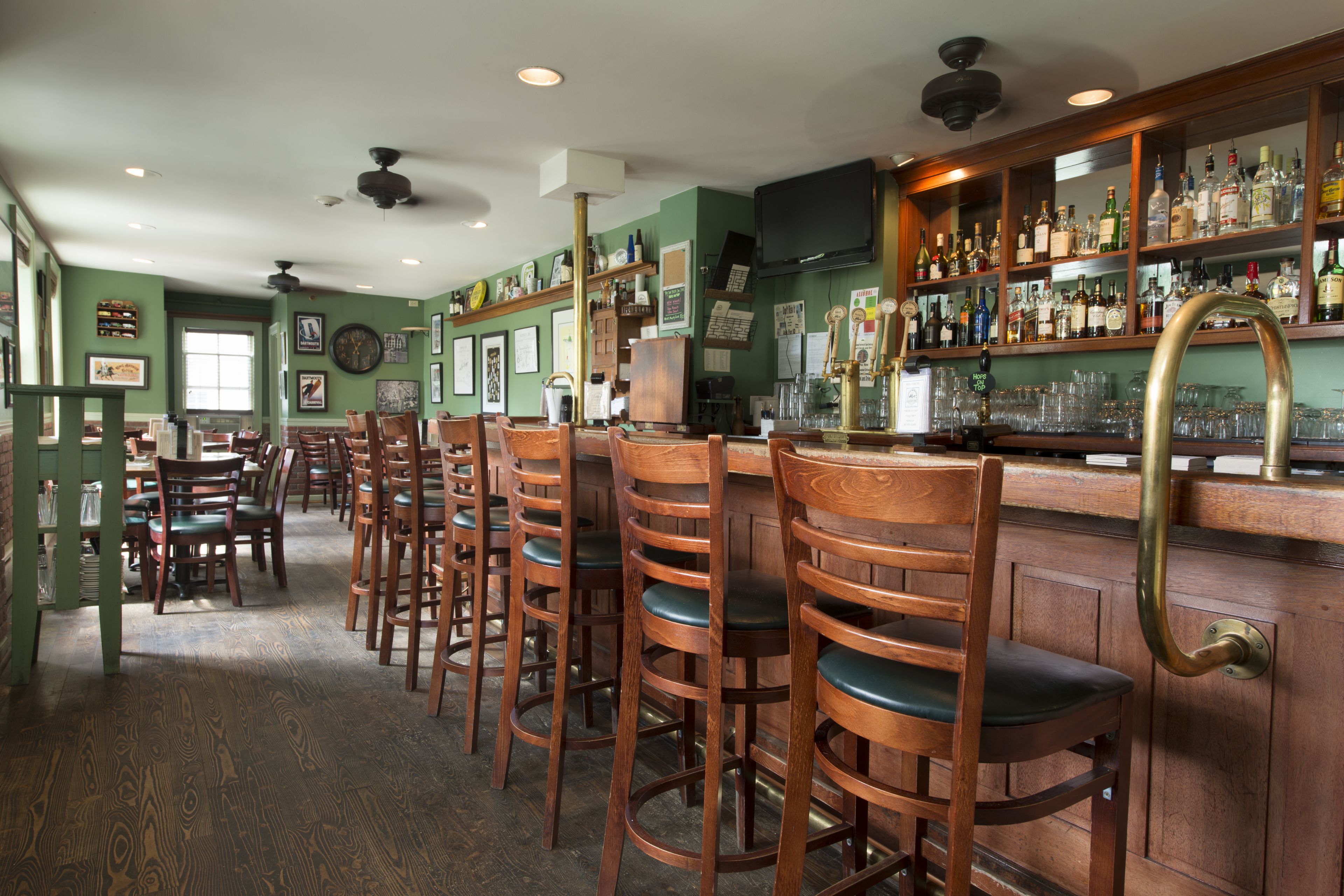 A bar area with wooden bar stools, a counter with various bottles, and a television mounted on the wall.