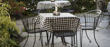 Outdoor tables with checkered tablecloths and metal chairs, surrounded by greenery.