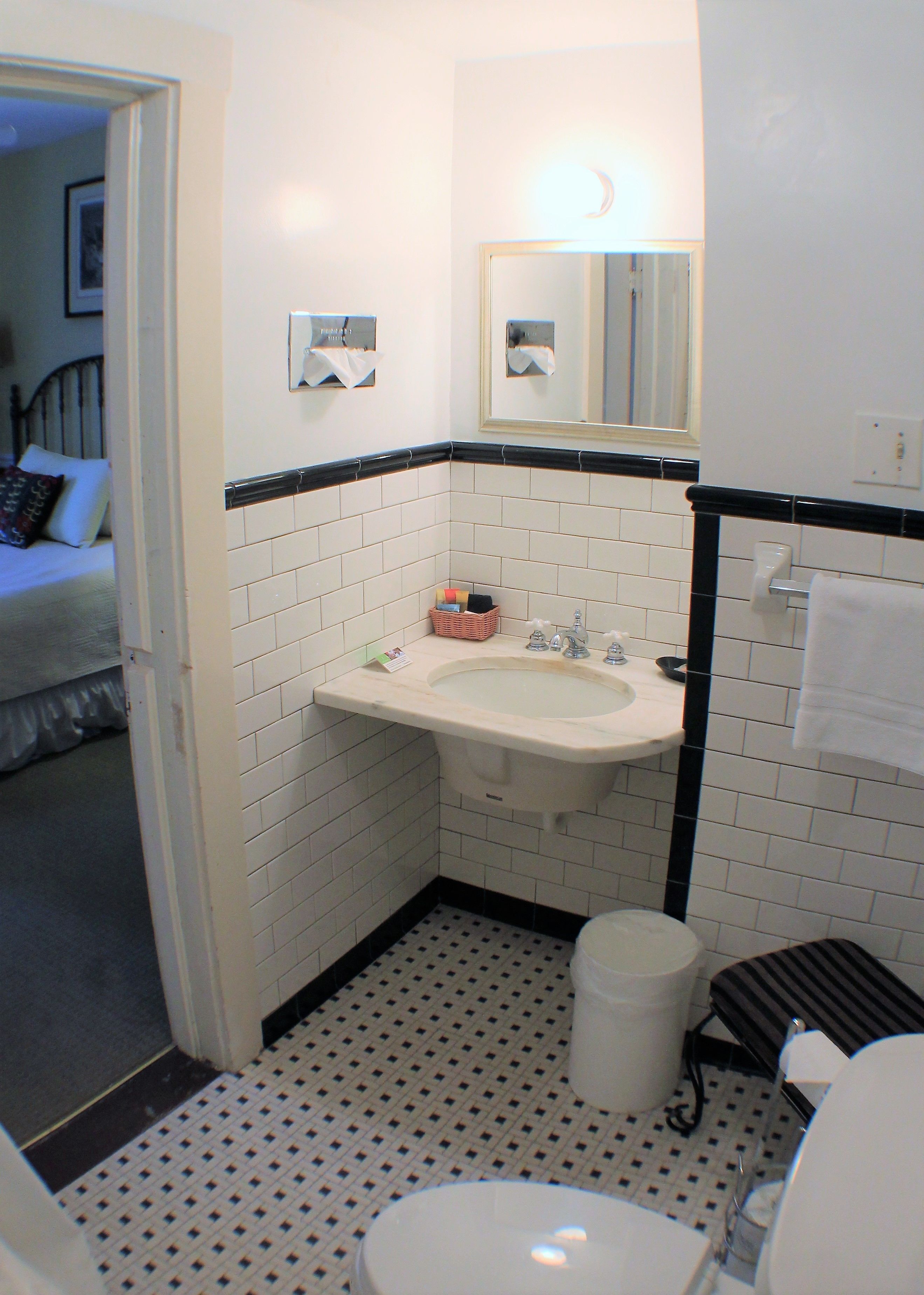 A bathroom with a white sink, a mirror, and a toilet. There is a small trash can and a basket with toiletries.