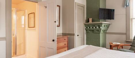 A bedroom with a bed, a dresser, a green brick fireplace, and a TV mounted on the wall.