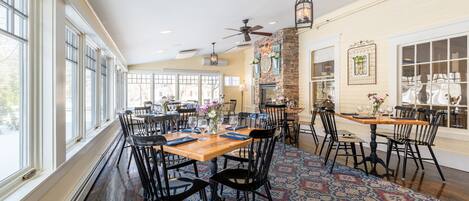 A spacious dining area with large windows, wooden tables, and black chairs.