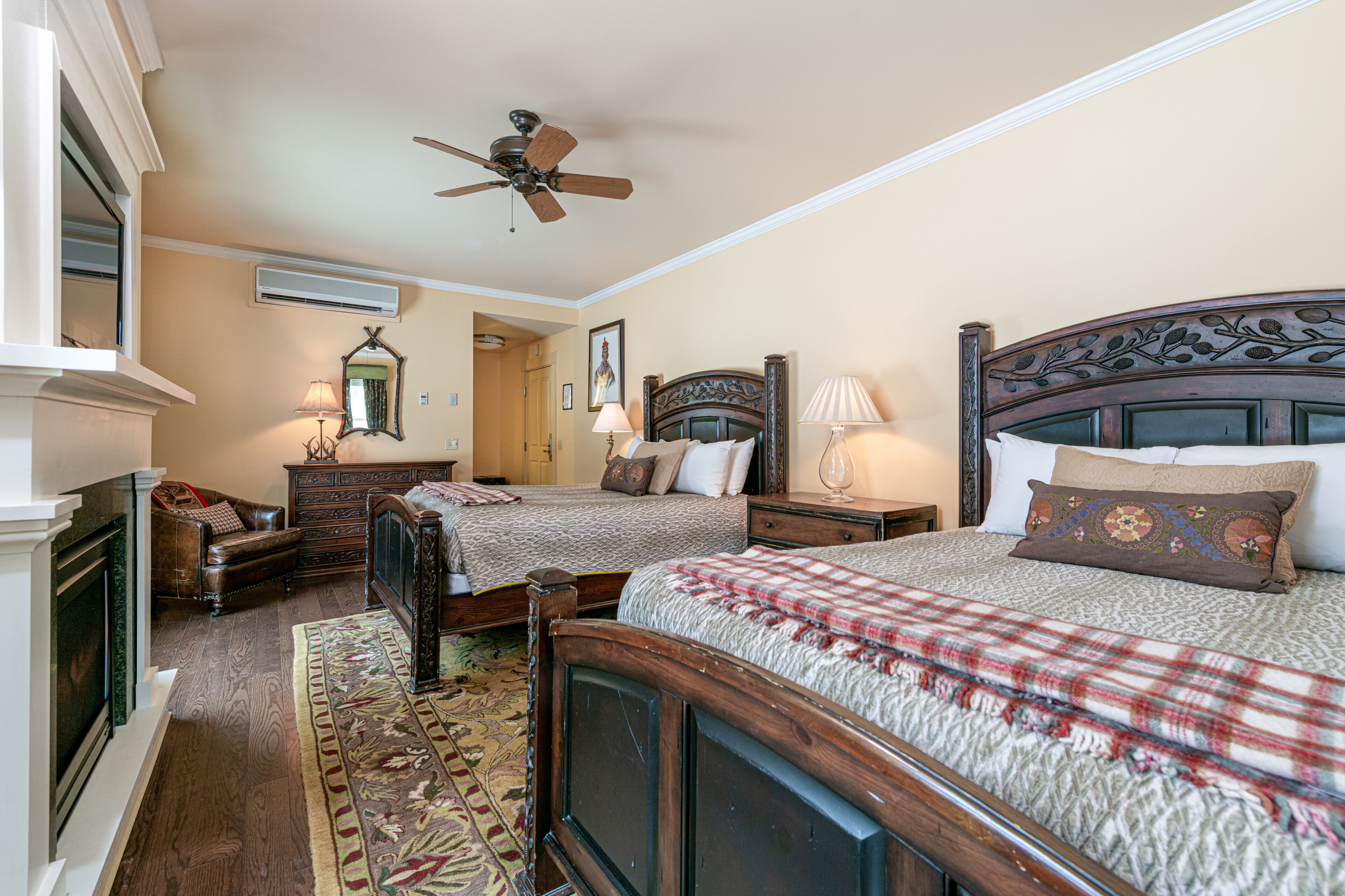 Un dormitorio con dos camas, ventilador de techo, chimenea y alfombra decorativa.