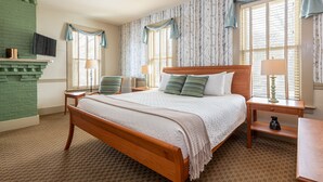 A neatly arranged bedroom with a wooden bed, two nightstands, a TV mounted on the wall, and a fireplace. - Norwich Inn (Norwich)