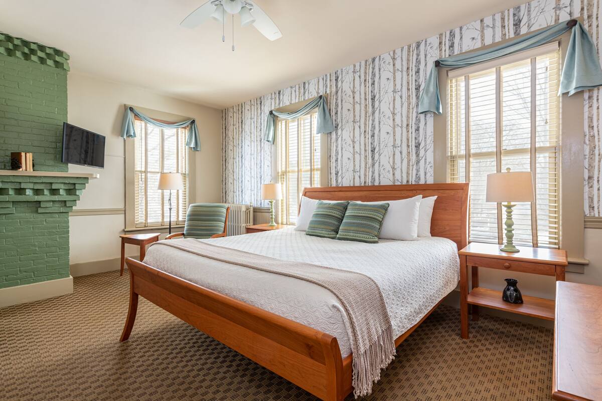A neatly arranged bedroom with a wooden bed, two nightstands, a TV mounted on the wall, and a fireplace.