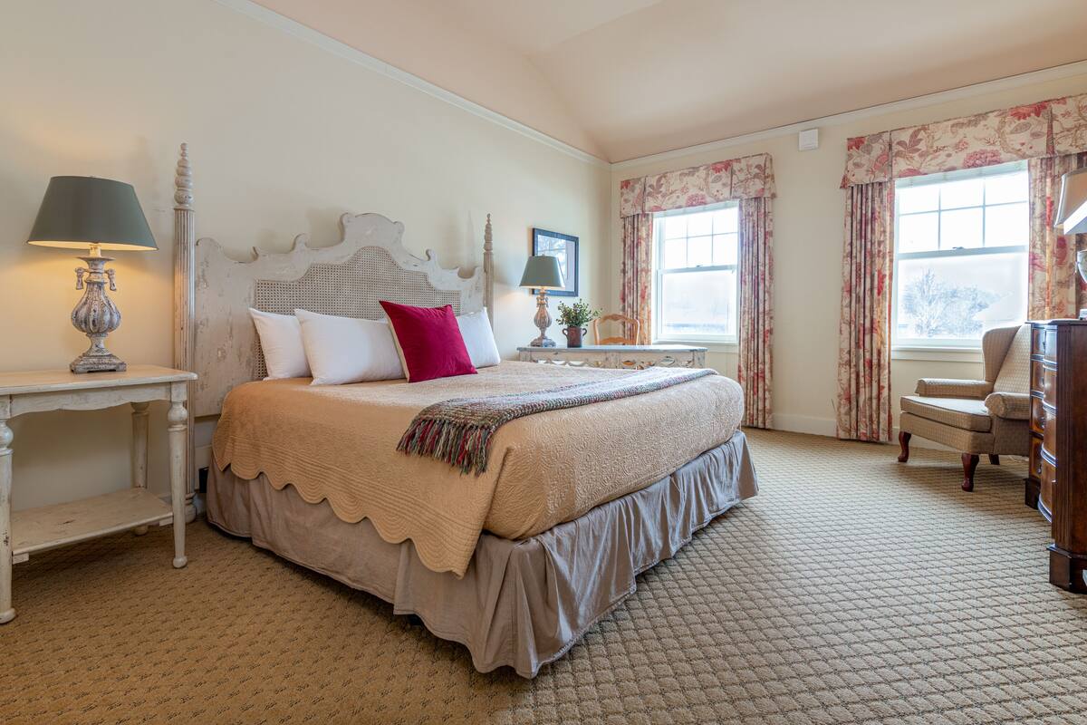 A bedroom with a large bed, a nightstand with a lamp, a dresser, and a chair.