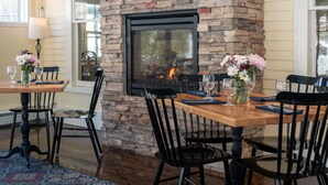 A dining area with a brick fireplace, wooden tables, black chairs, and floral centerpieces. - Norwich Inn (Norwich)